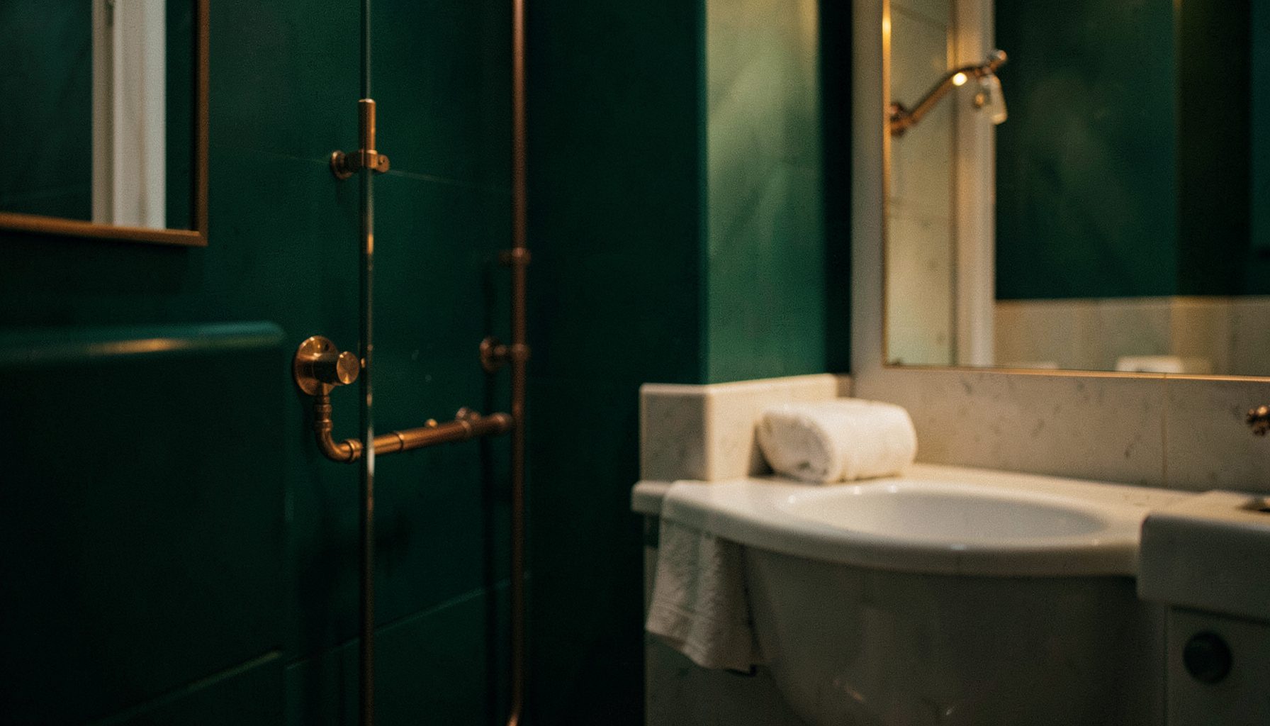 A warm, softly lit residential bathroom with copper plumbing fixtures and a deep green accent wall, shallow depth of field